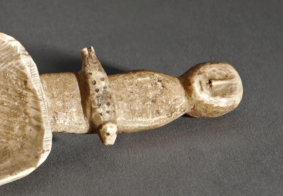 Detail eines Opferlöffels der Korjaken Detail eines aus Walrosszahn geschnitzten Löffels. Am Griff ist eine Figur dargestellt.
