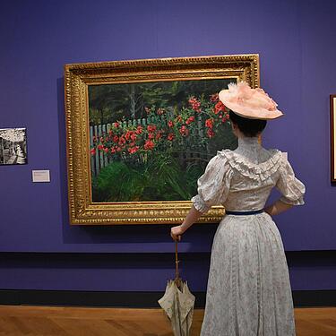 Besucherin in Kostüm betrachtet ein Gemälde mit Blumen