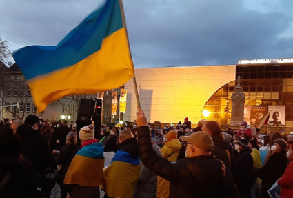 Kundgebung bei Demonstration, im Vordergrund schwenkt jemand eine Ukraine-Fahne