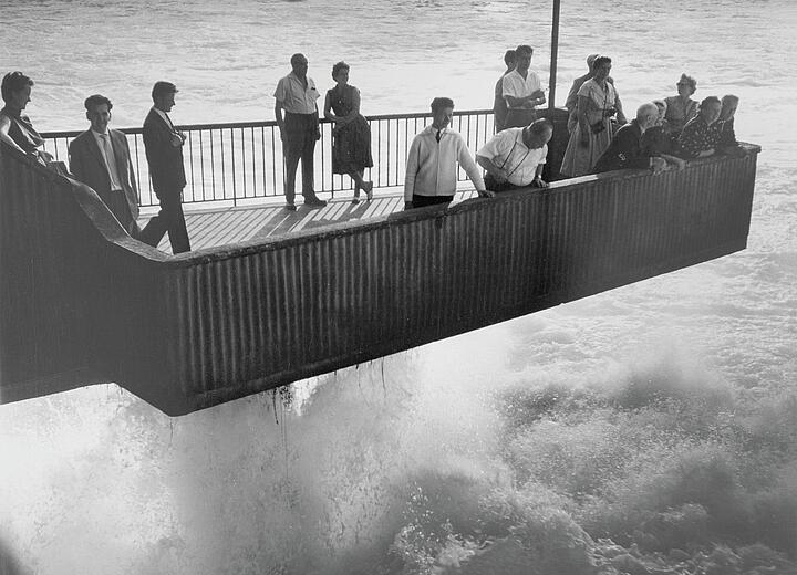 Schwarz-Weiß-Fotografie aus den 190er Jahren: Mehrere Personen stehen auf einer Aussichtsplattform, unter ihnen tosendes Wasser