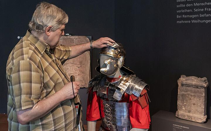 Ein Mann ertastet den Helm einer Figurine mit römischer Legionäruniform Ein Mann ertastet den Helm einer Figurine mit römischer Legionäruniform