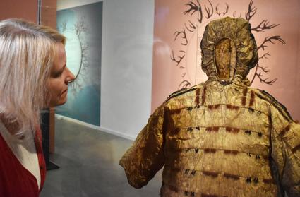 Blick in die Sonderausstellung „Schamanen Sibiriens“ Frau betrachtet in einer Vitrine einen beigfarbenen Anorak, der aus Darmhaut gefertigt wurde.