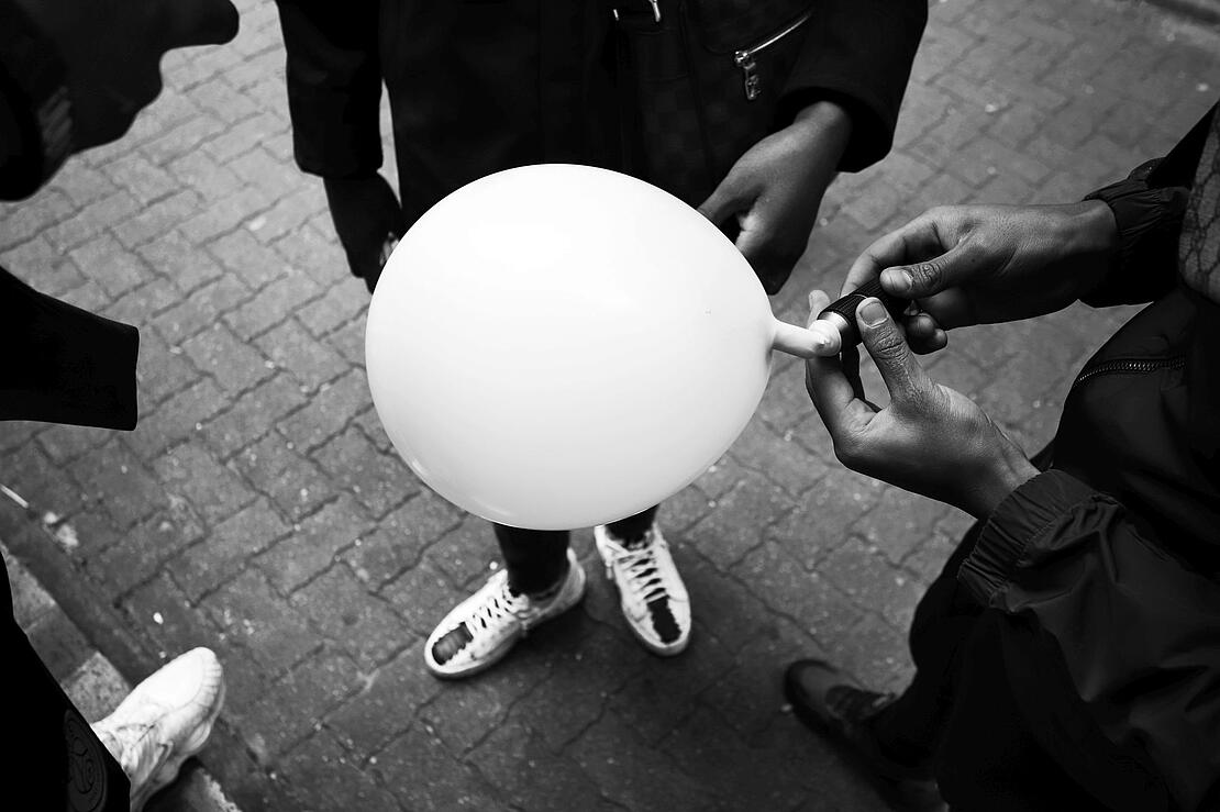 Schwarz-Weiß-Aufnahme zeigt einen hellen Luftballon, umringt von mehreren Personen, von denen man die Köpfe nicht sieht