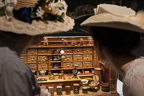 Zwei Besucherinnen in historischem Kostüm betrachten einen Kaufladen aus dem 19. Jahrhundert