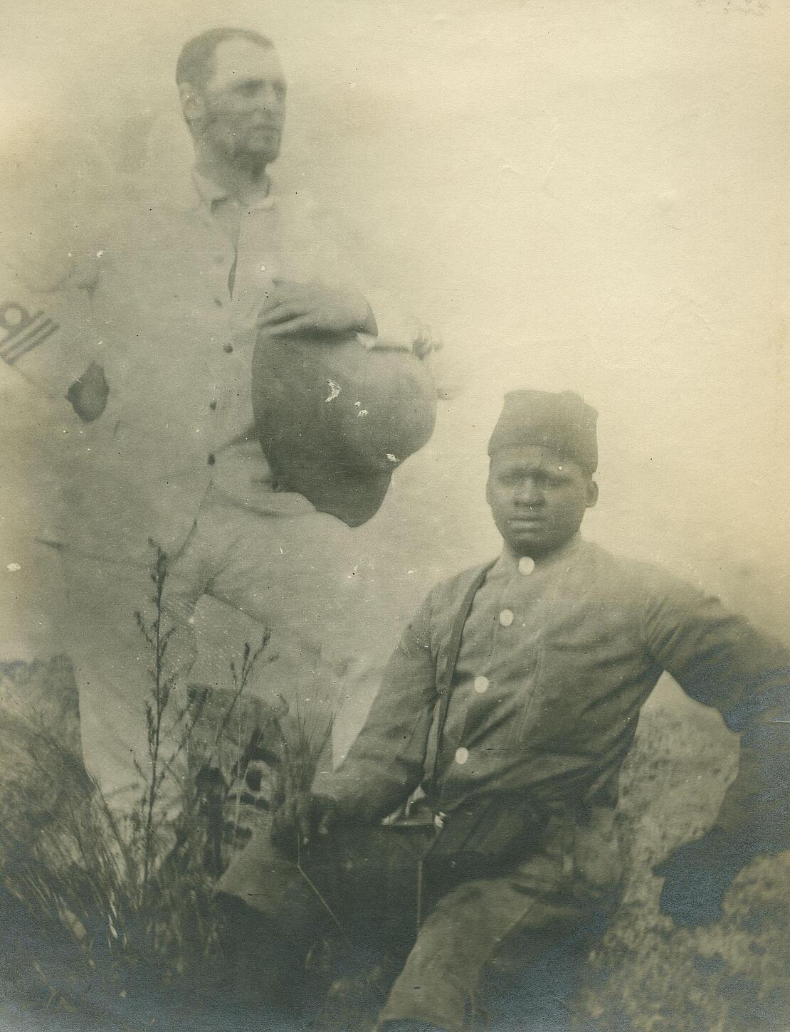 Historische Fotografie zeigt links stehenden Mann in Uniform und rechts daneben sitzend farbigen Diener