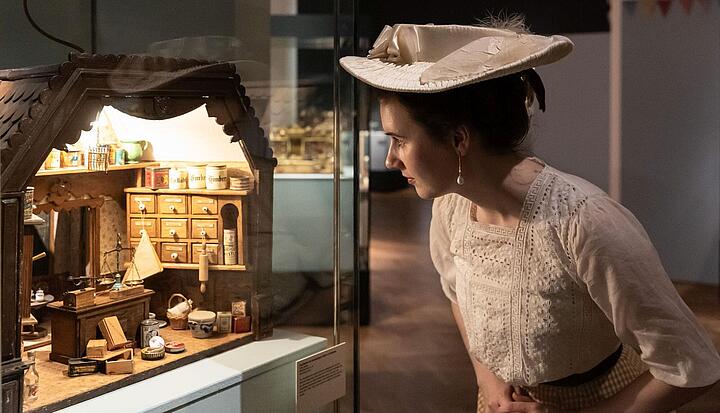 Frau betrachtet in einer Vitrine einen Kaufladen Frau betrachtet in einer Vitrine einen Kaufladen