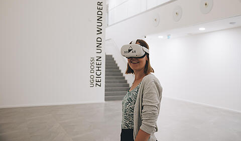 Frau trägt eine VR-Brille und steht in einem großen weißen Raum