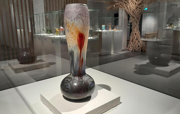 Blick in einen Ausstellungsraum, im Vordergrund schmale Vase mit roten Krokosblüten