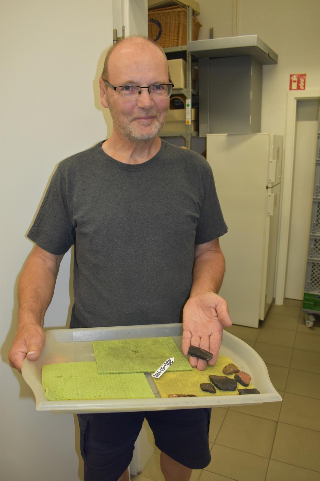 Dr. Klaus Wirth mit ersten Funden Ein Mann hält ein Tablett mit kleinen archäologischen Funden