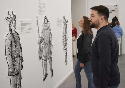 Mehrere Personen betrachten an einer Wand lebensgroße Zeichnungen von drei Schmanenfiguren