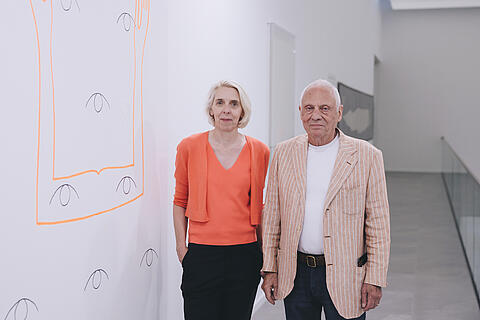 Kuratorin Gabriele Pieke steht neben dem Künstler Ugo Dossi in der Ausstellung