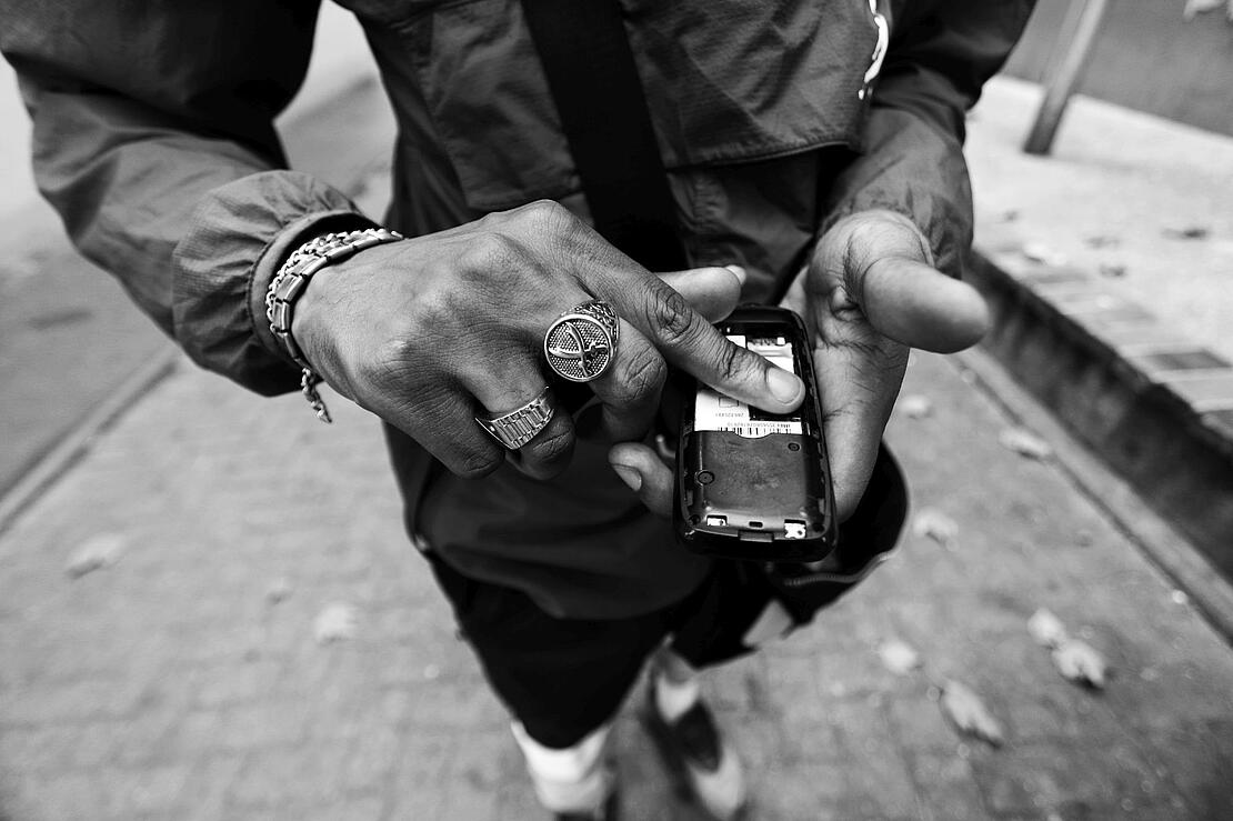 Schwarz-weiß-Aufnahme zeigt die Hände eines farbigen Mannes, der ein Handy hält und mehrere Ringe trägt