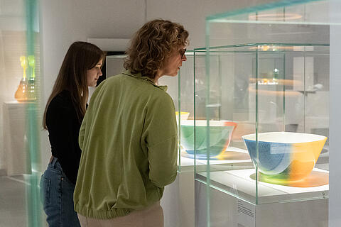 Besucherinnen der Ausstellung "Herzklopfen" betrachten Glaskunst-Objekt
