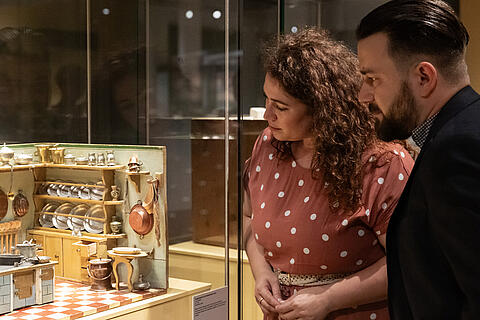 Zwei Besucher in der Ausstellung betrachten eine Puppenküche