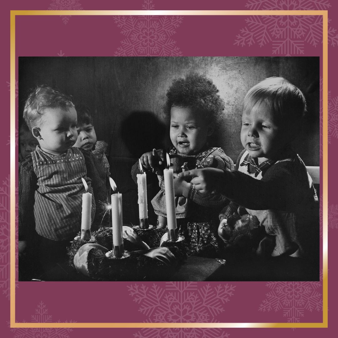 Ein schwarz-weiß Foto von drei kleinen Kindern vor einem Adventskranz.
