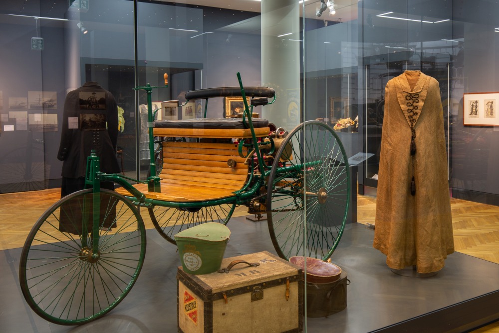 Blick in die Ausstellung „Belle Époque“: Rechts neben dem Benz-Mobil sehen Sie einen Reisemantel aus dem Ende des 19. Jahrhunderts 