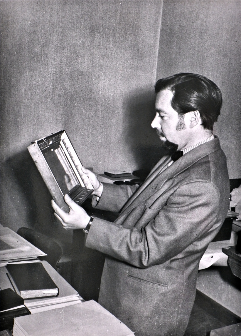 Helmut Gernsheim mit der Heliographie Helmut Gernsheim trägt einen Anzug und hält einen Bilderrahmen mit einer Fotografie schräg.